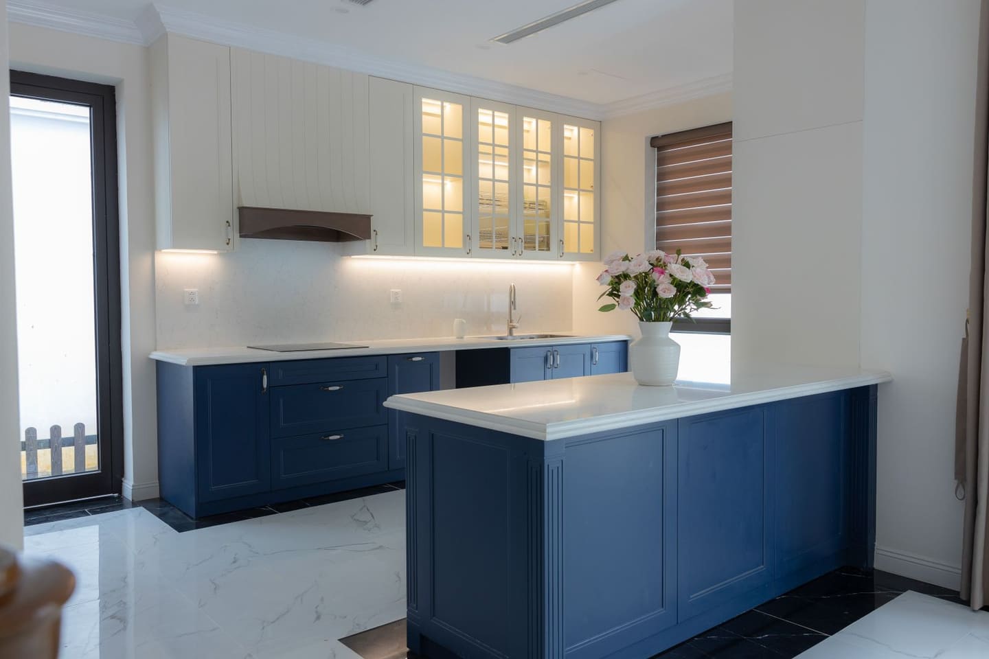 A finished in-frame kitchen with navy-blue painted cabinetry, cream wall units and a light quartz worktop around a central island.