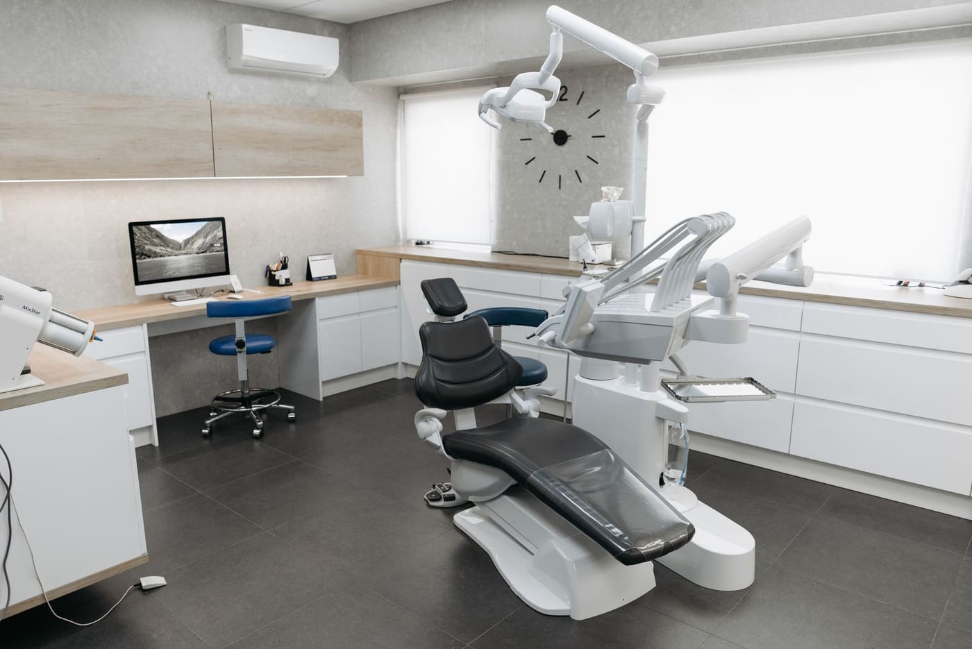 A bright, modern dental surgery room with wood-toned cabinetry, a reclined dental chair and an overhead operating light.