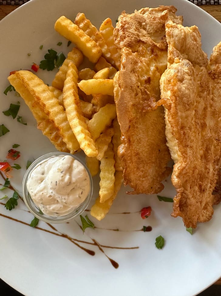 A freshly fried, golden battered fish fillet served with chips and tartar sauce