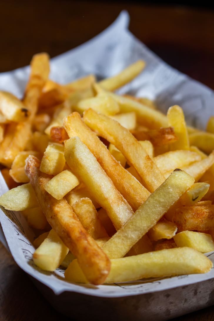 A pile of golden, freshly fried chips in a paper-lined tray