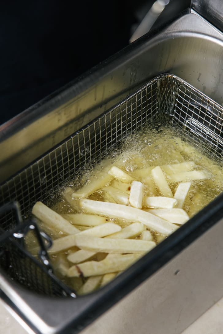 Chips frying in a wire basket in a stainless steel fryer, oil bubbling