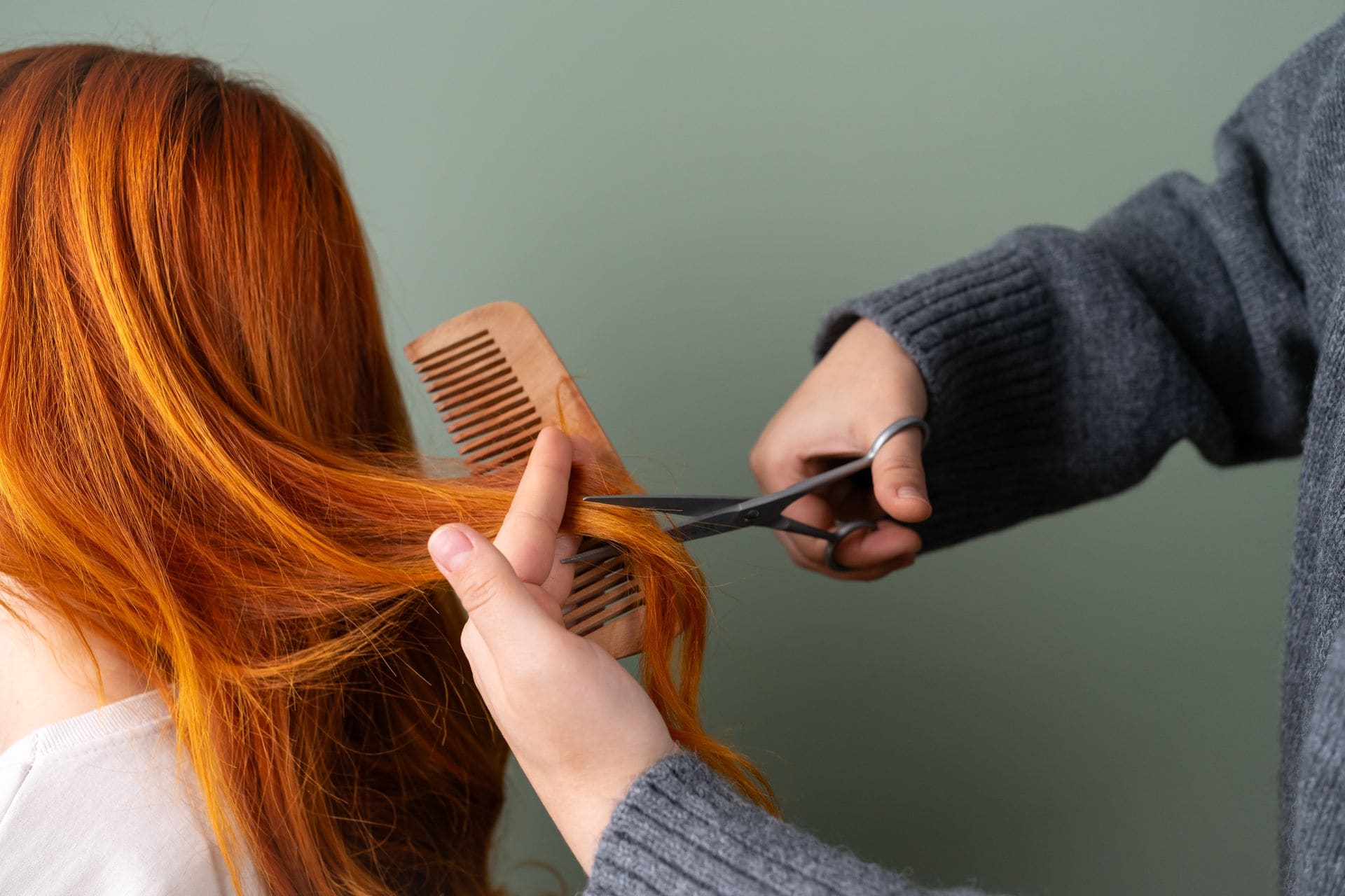 A stylist sectioning and trimming a client's copper-red hair with a wooden comb